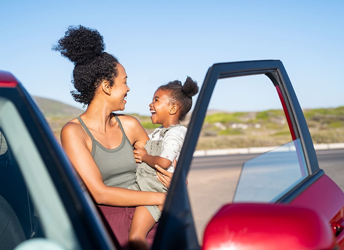 Contact - Cheerful Mother Holding her Daughter While Standing Next to her Red Car During a Road Trip